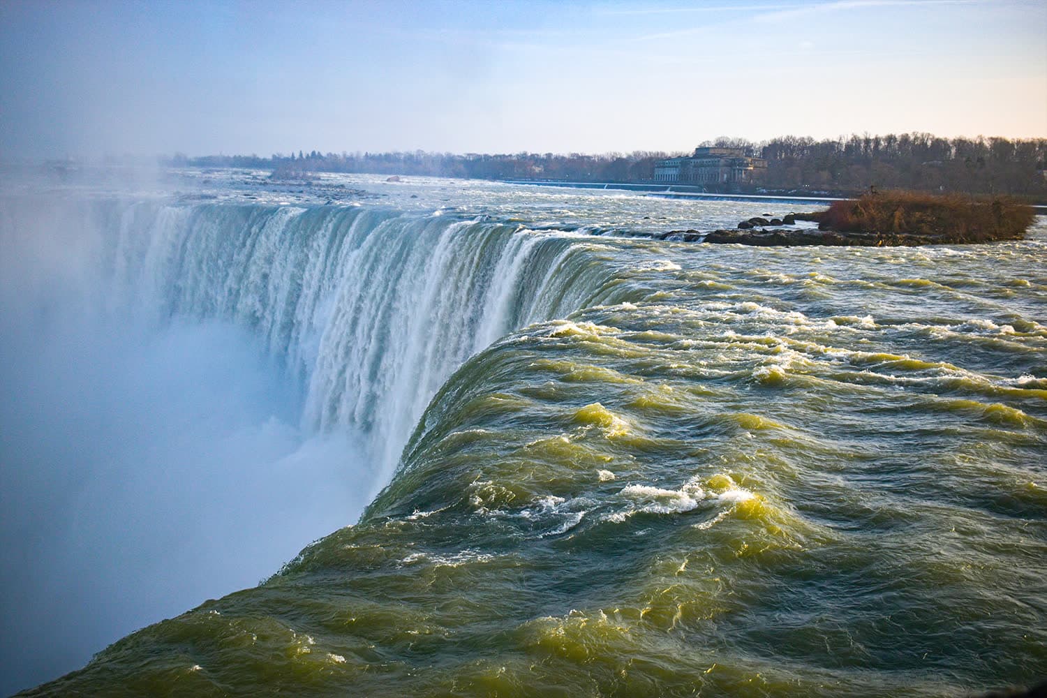 Green water sliding over the curved lip of Niagara Falls into rising mist.