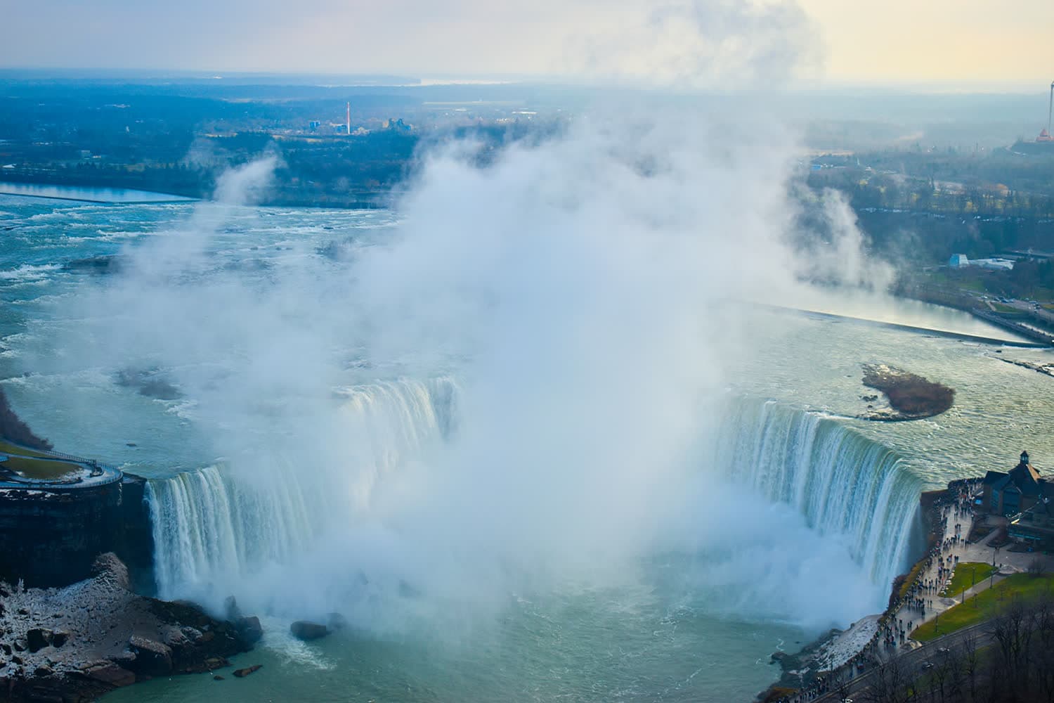 Niagara Falls seen from above, with a tall column of white mist rising out of the horseshoe.