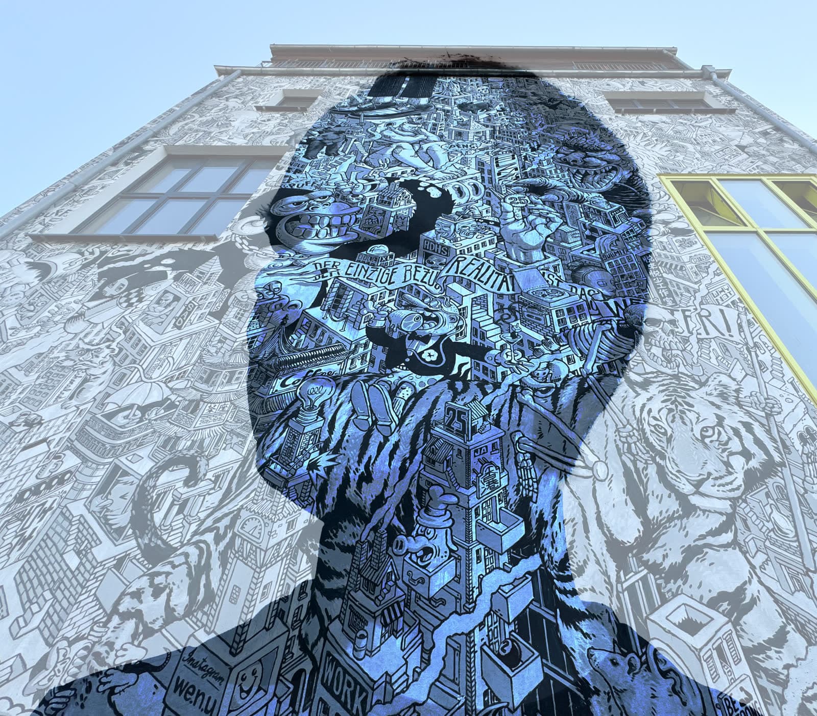 A large mural of a face on the side of a building, filled with dense blue and black line drawings.